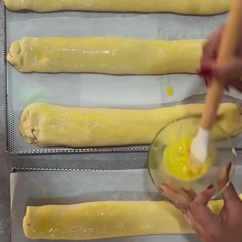 Une main dore au pinceau des roulés de pâte feuilletée sur une plaque